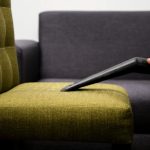 Close-up of a person vacuuming a modern sofa chair indoors, highlighting cleaning service.